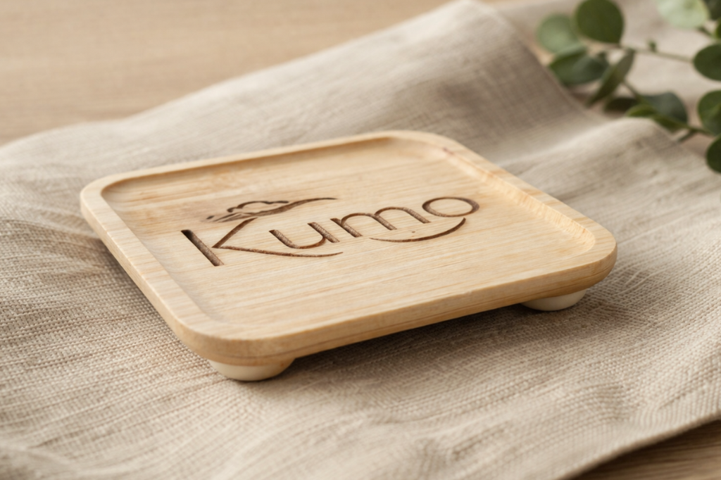 Bamboo coaster with 'Kumo' branding on a beige fabric surface